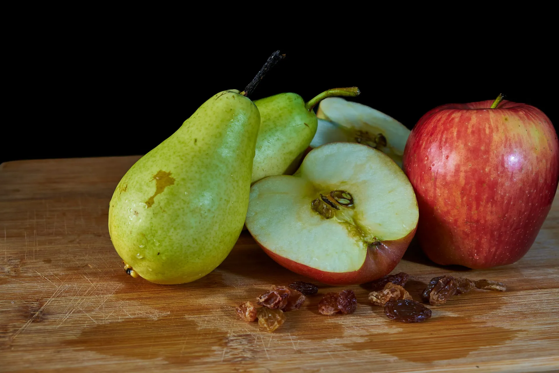 Twee groene peren, een doorgesneden appel en een rode appel op een houten snijplank