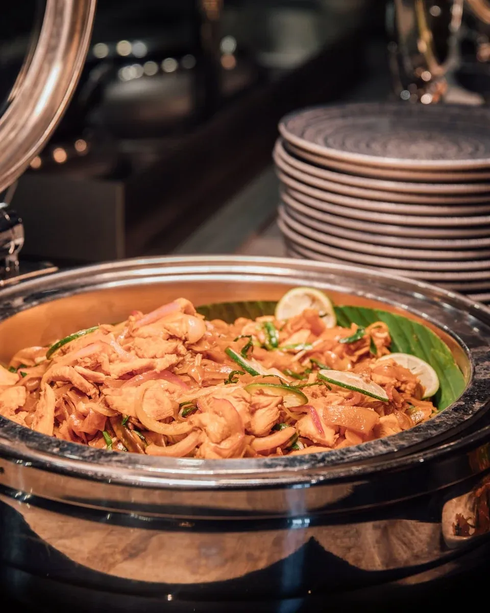 Open warmhoudschaal met kip, ui en limoen op een warm buffet, borden erachter