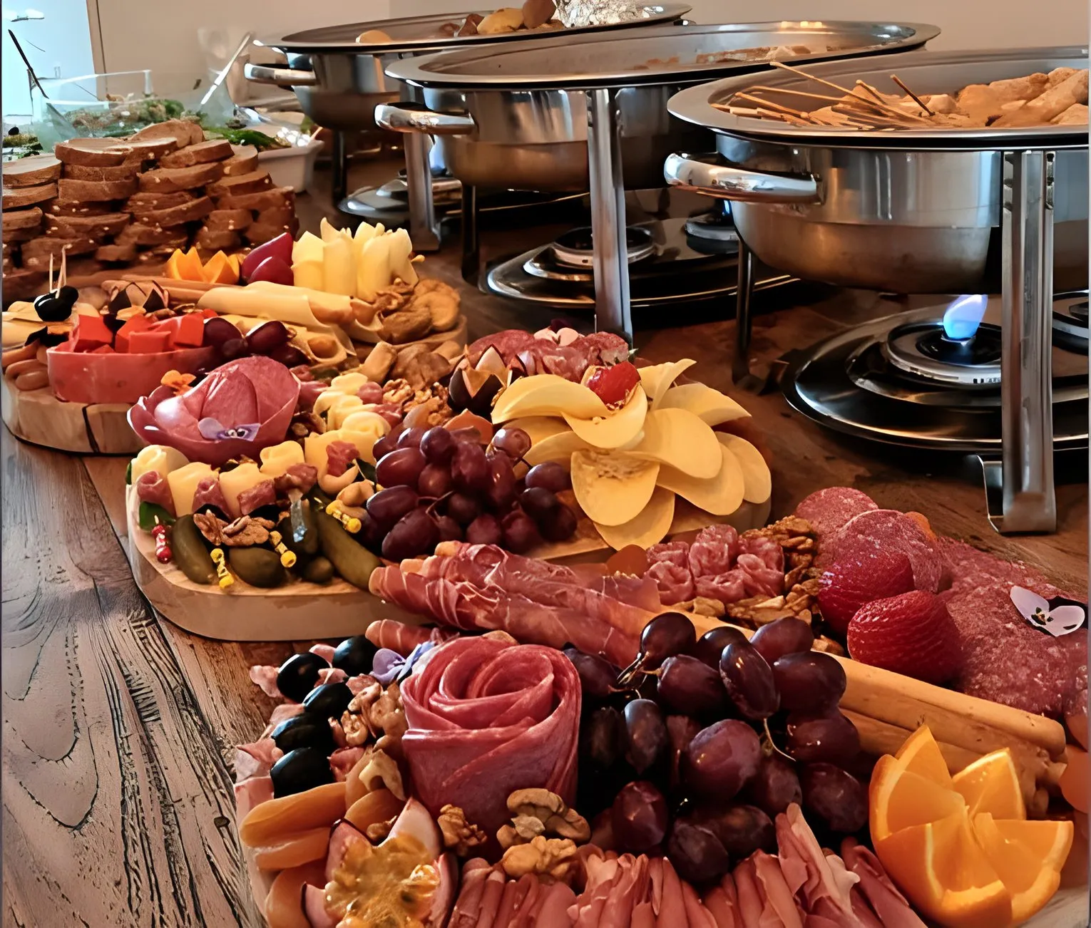 Lange tafel met borrelplanken, met daarachter een warm buffet in chafing dishes
