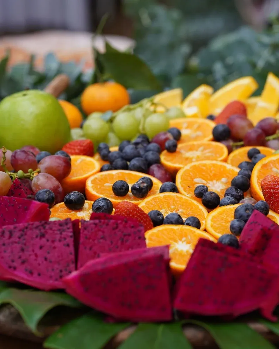 Kleurrijke fruitschaal met sinaasappel, blauwe bessen, pitaya, druiven, aardbeien en appels op bladeren