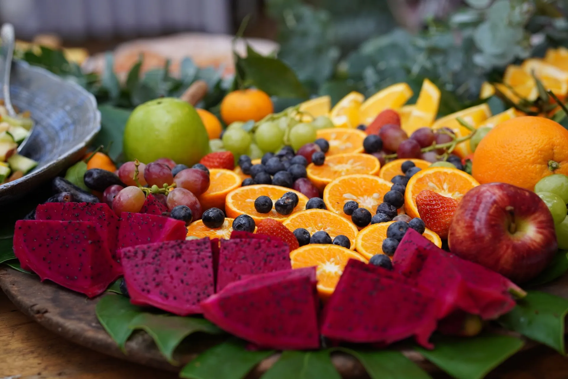 Kleurrijke fruitschaal met sinaasappel, blauwe bessen, pitaya, druiven, aardbeien en appels op bladeren