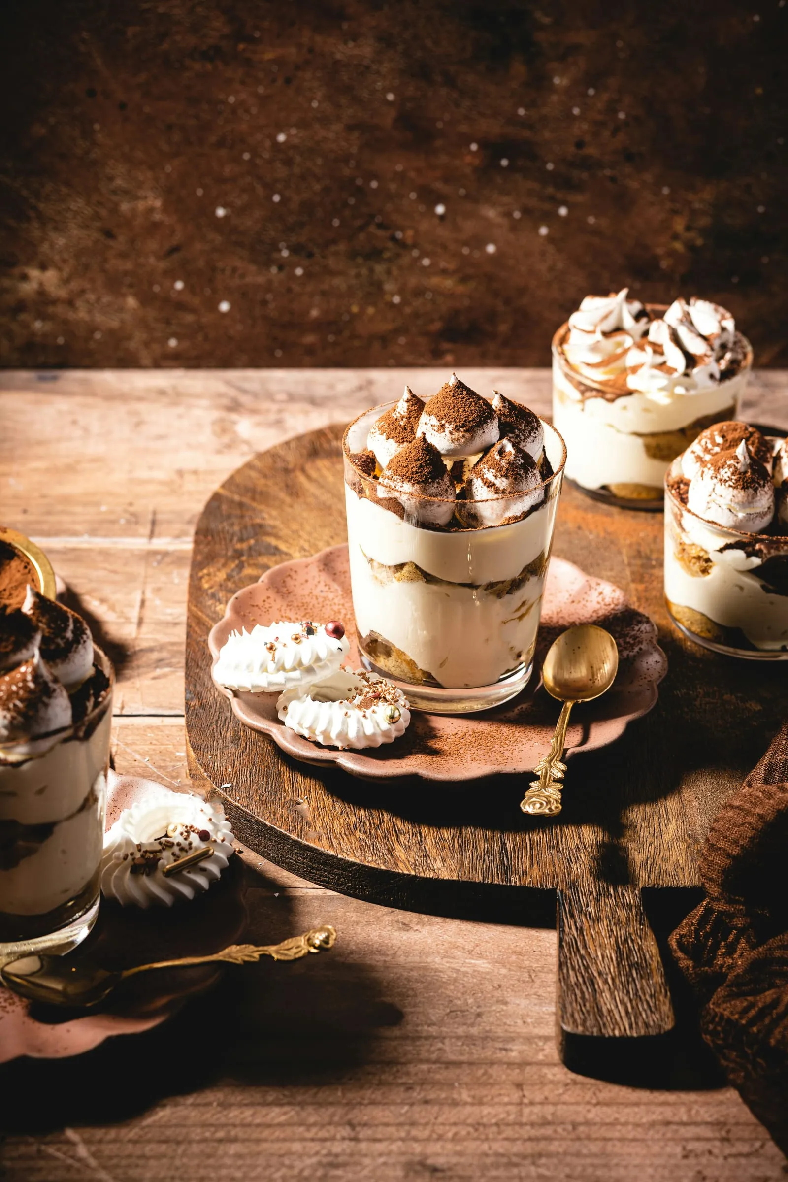 Tiramisu in losse glaasjes op een houten plank, met cacao en kleine schuimpjes