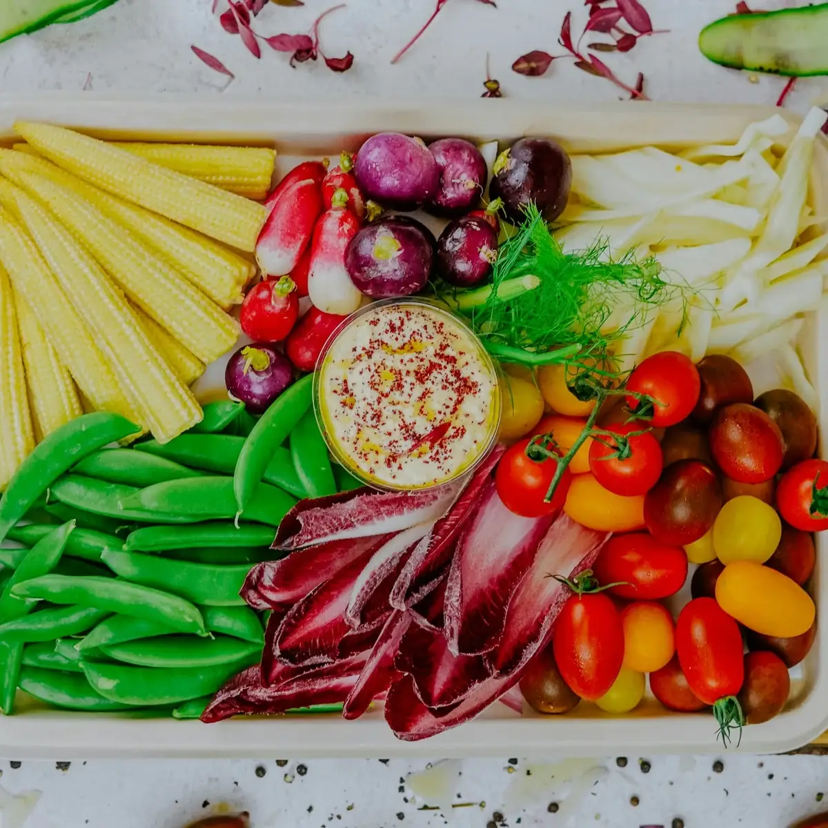 Kleurrijke rauwkostschaal met peultjes, radijsjes, tomaatjes, rode witlof en een dip