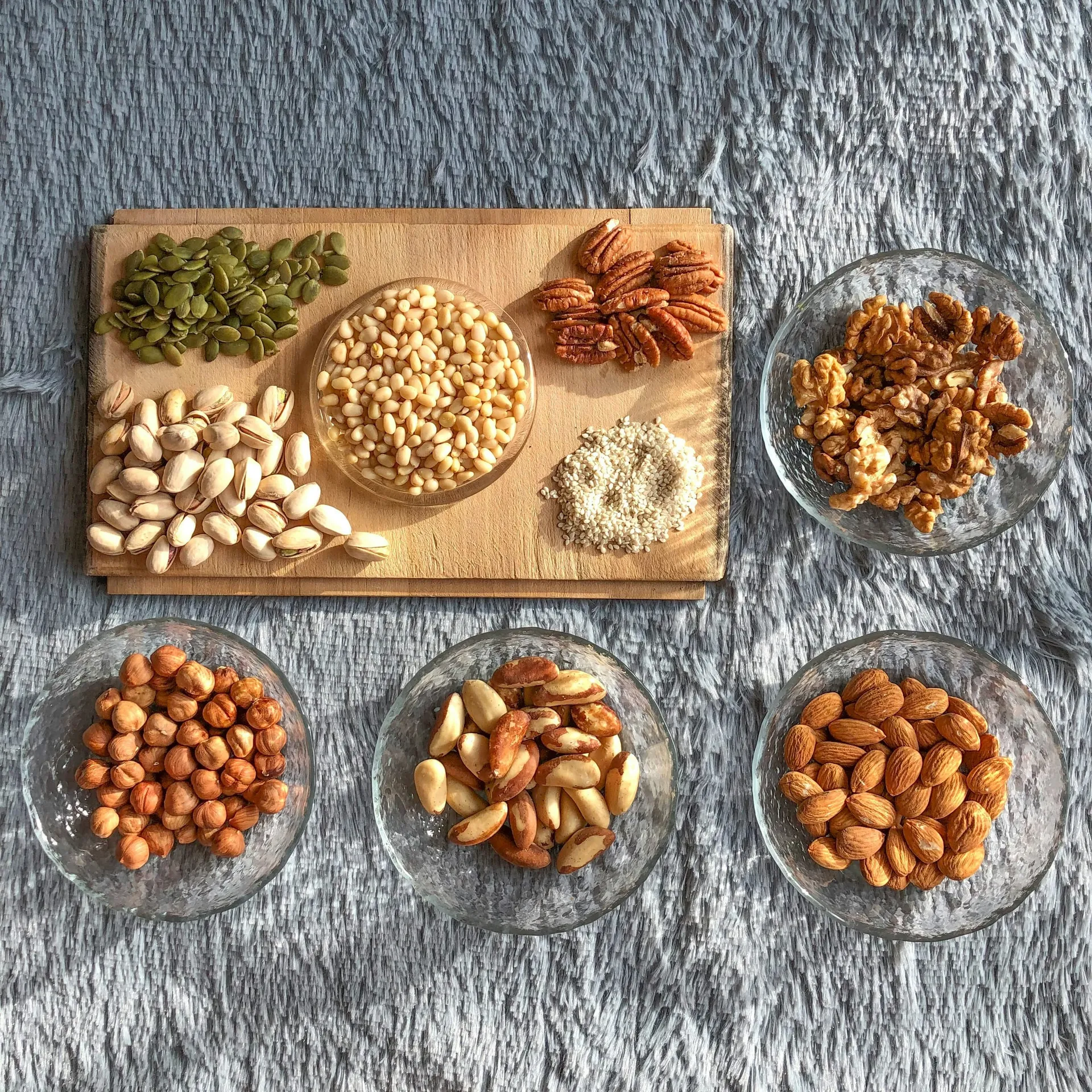 Pistachenoten, pecannoten, walnoten, hazelnoten, paranoten, amandelen, pijnboompitten, pompoenpitten en sesamzaad in glazen schaaltjes