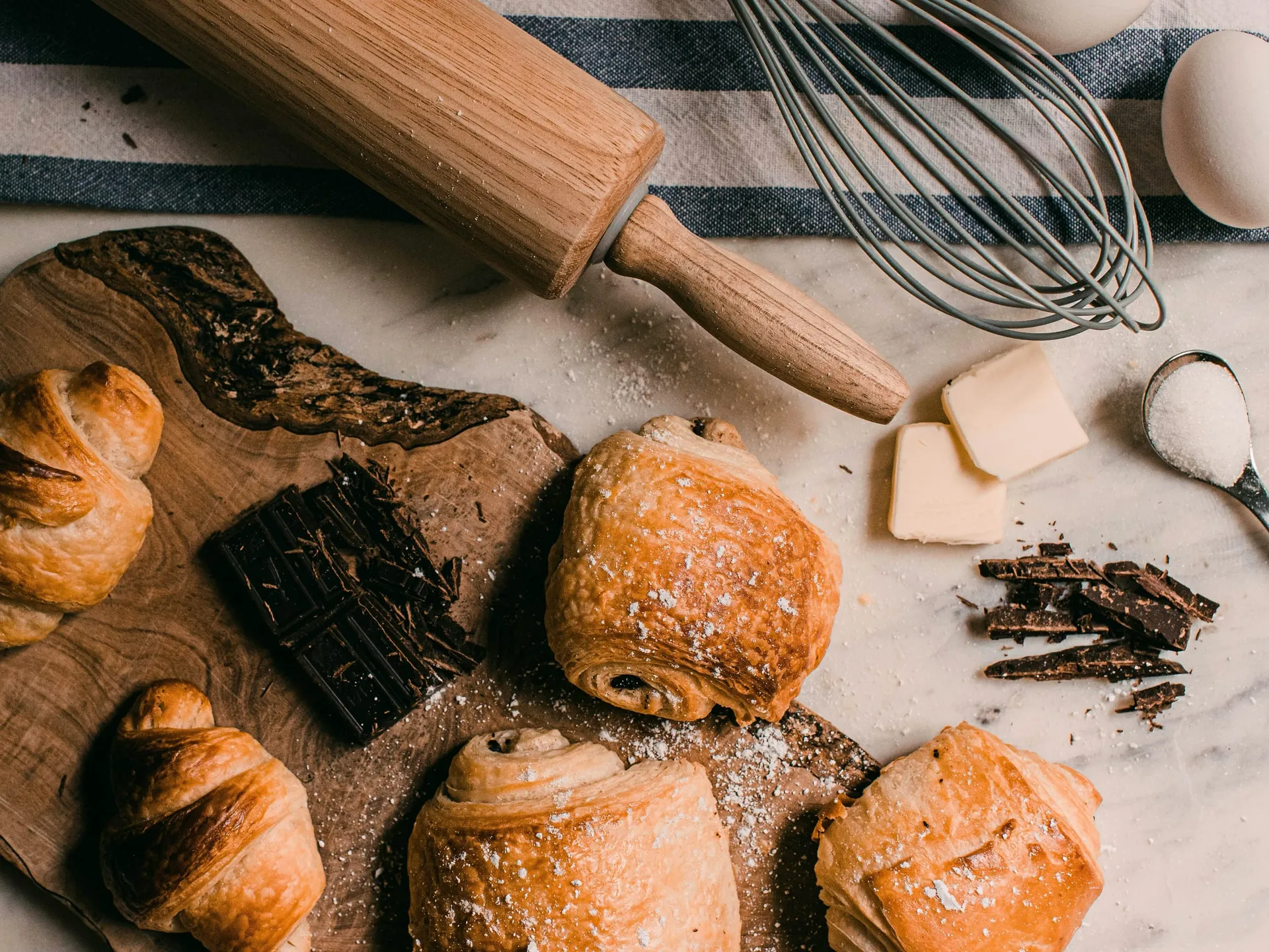 Croissants en chocoladebroodjes op een houten plank, met boter, eieren, chocolade en een deegroller