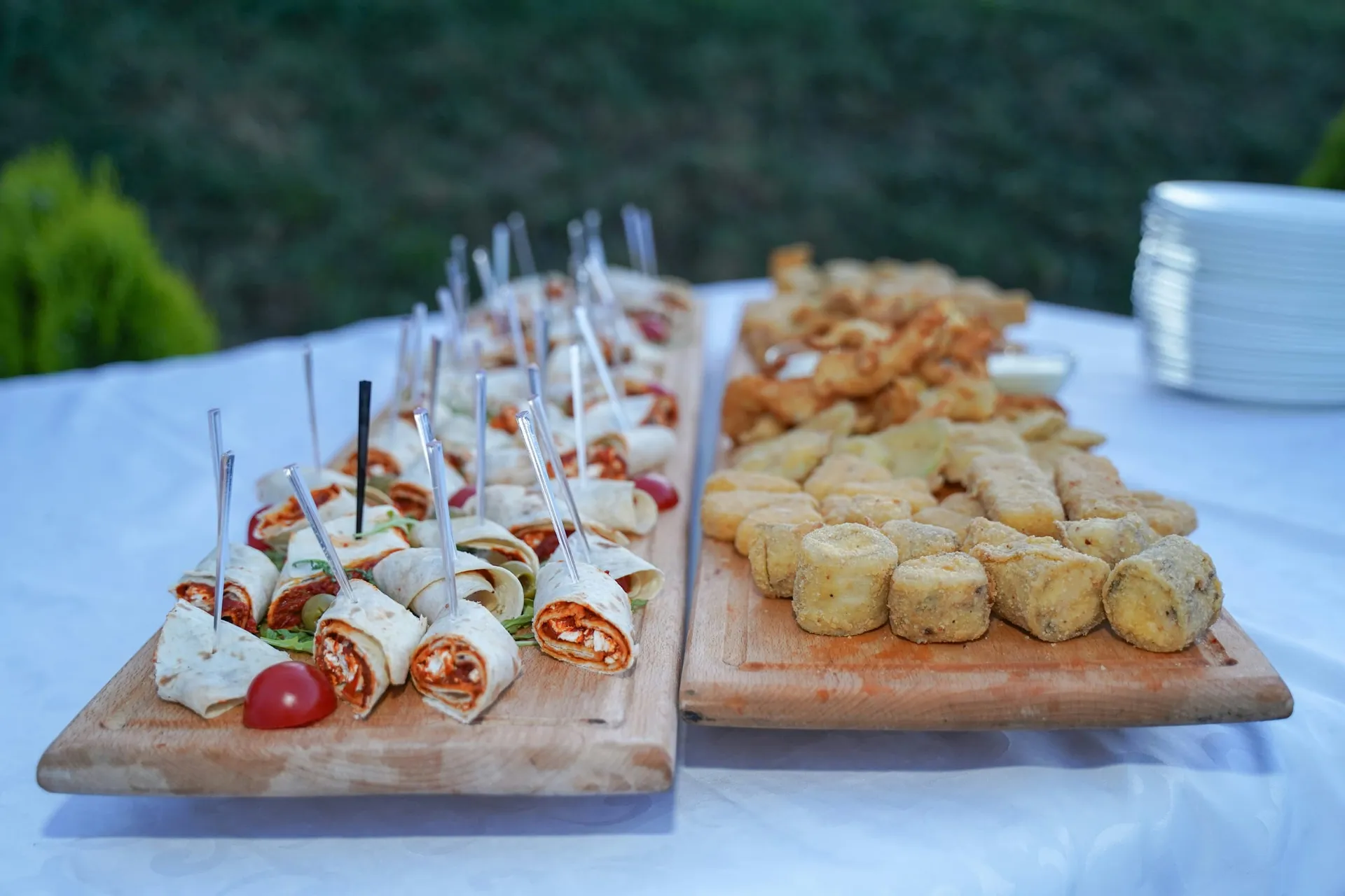 Houten planken met wraps op prikkers en gefrituurde hapjes op een tafel in de tuin
