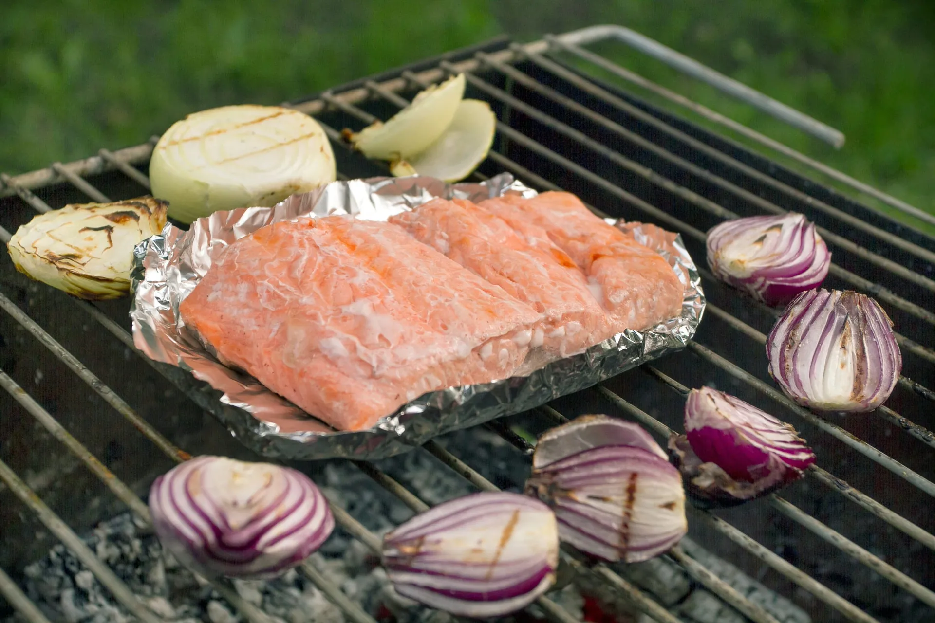 Zalmfilet in een bakje van aluminiumfolie op de barbecue, met gegrilde rode en witte uien
