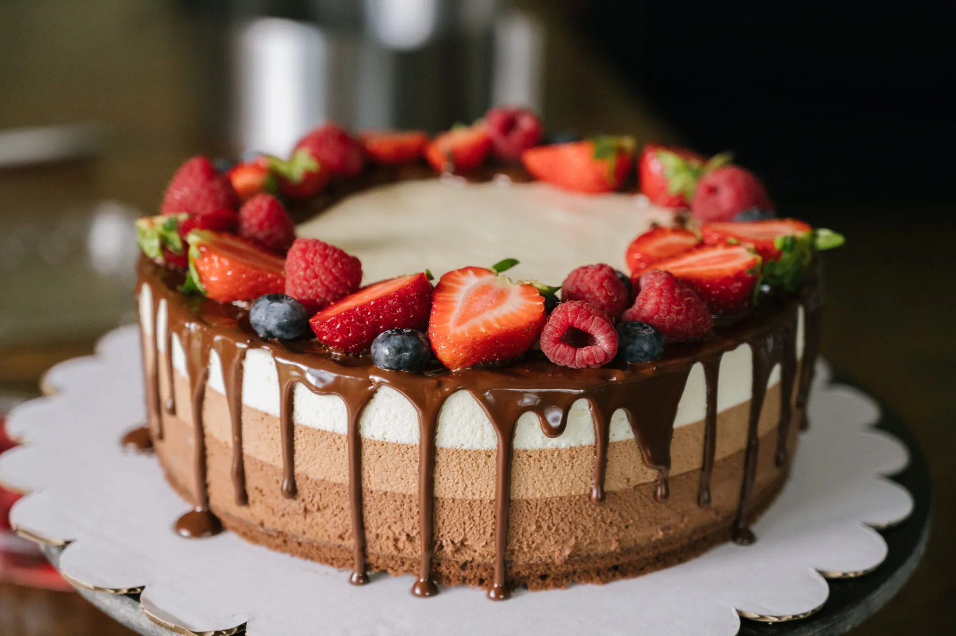 Chocolademoussetaart in drie lagen met chocoladedrip en een krans van aardbeien, frambozen en blauwe bessen