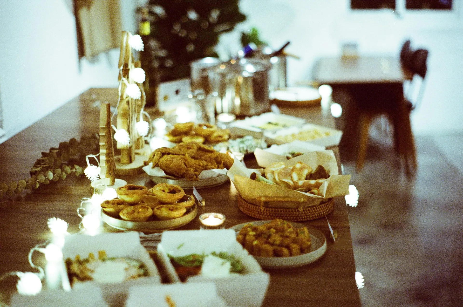 Een lange feesttafel met eiertaartjes, gefrituurde kip en lichtjes aan het eind van de avond