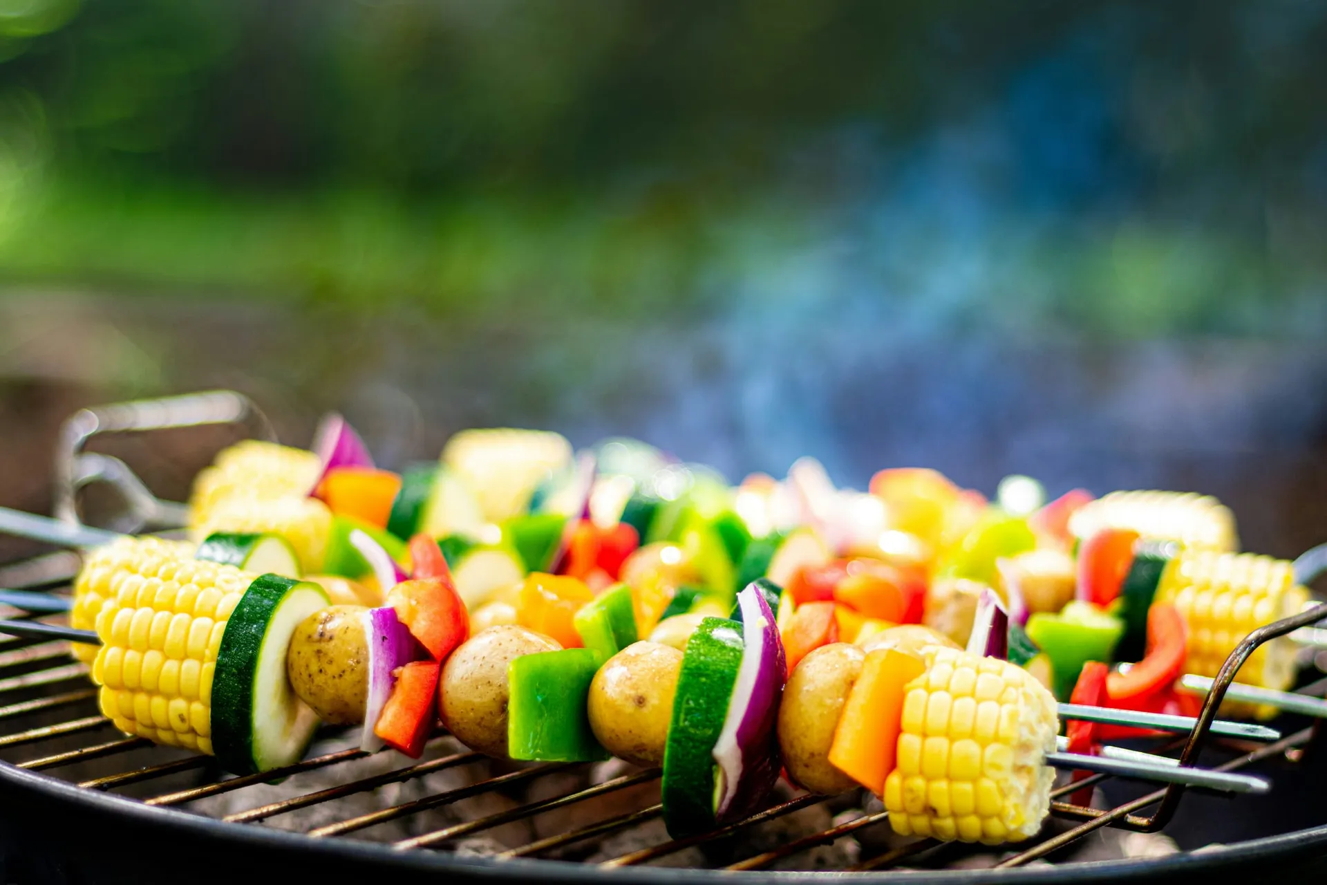 Groentespiesen met maïs, courgette, paprika, rode ui en krieltjes op een barbecue in de tuin