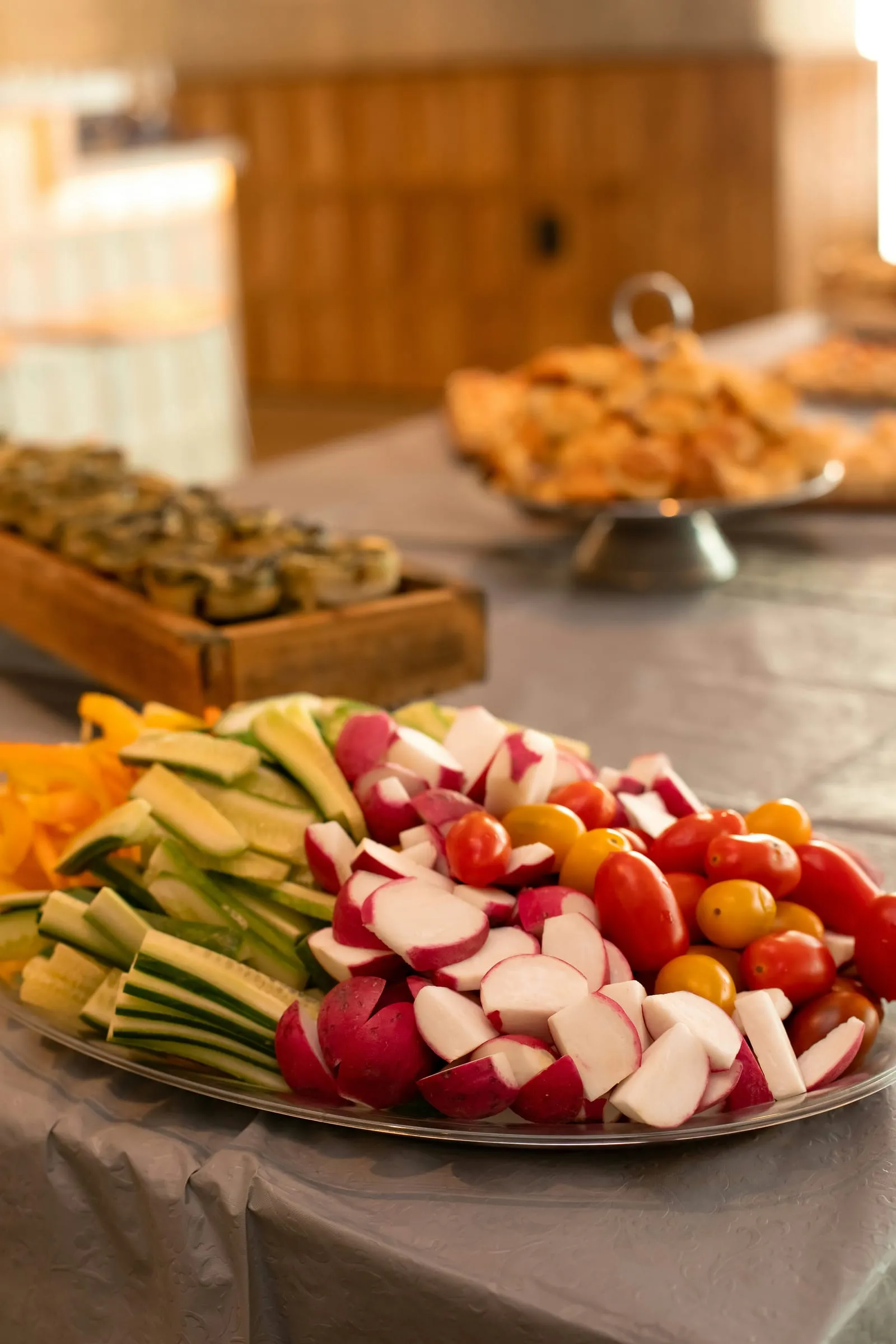 Schaal met reepjes komkommer, radijs, paprika en tomaatjes op een buffettafel met hapjes erachter