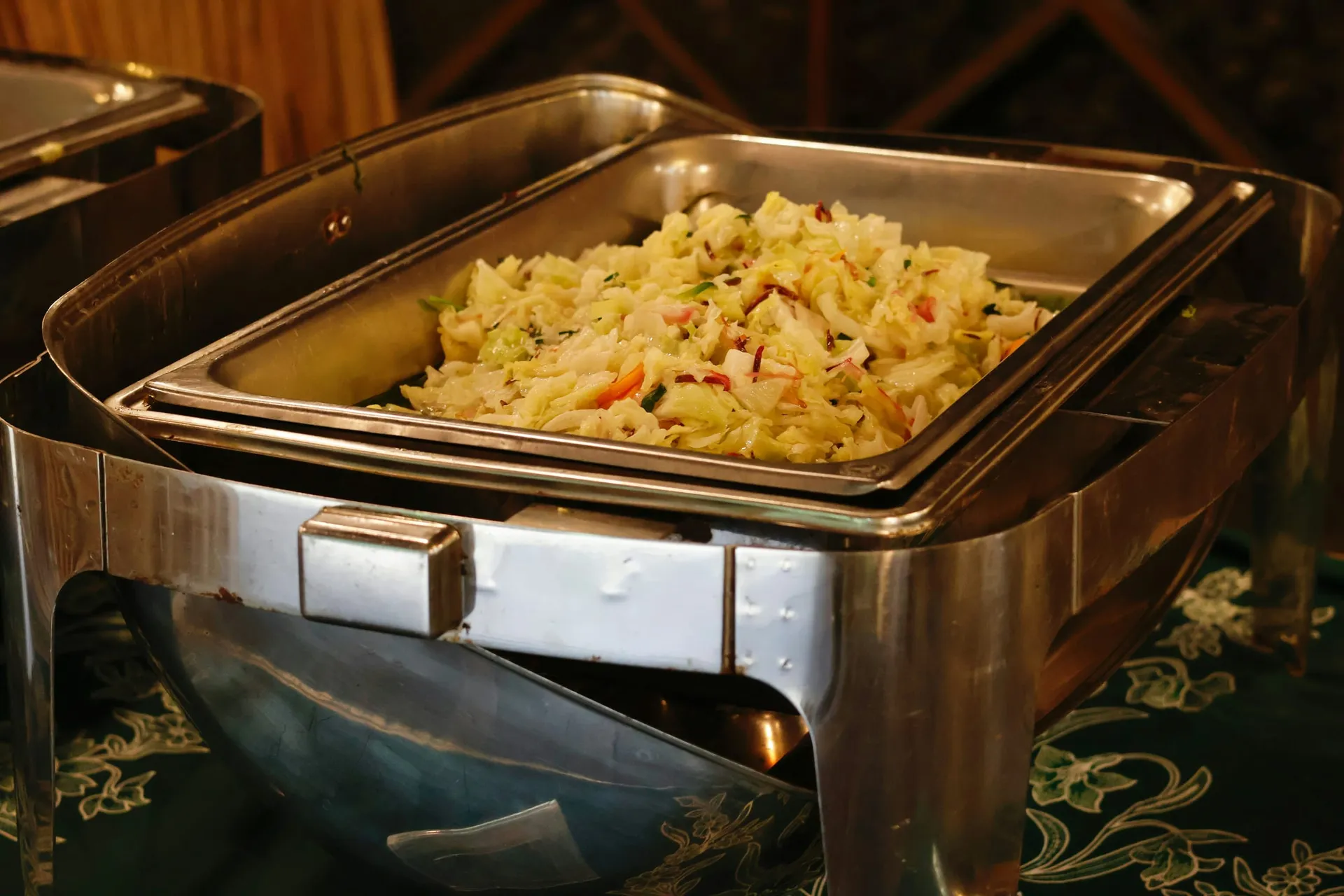 Een chafing dish met gestoofde witte kool op een buffettafel met een groen tafelkleed